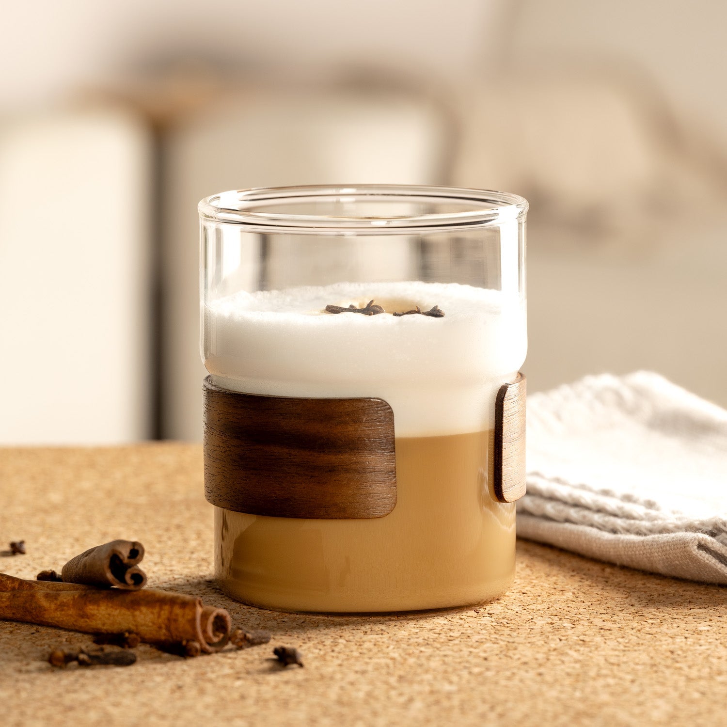 Kaffeespezialität mit Milchschaum und Gewürzen in einem Glas mit Holzmanschette, stilvoll serviert auf einem Korkuntergrund.