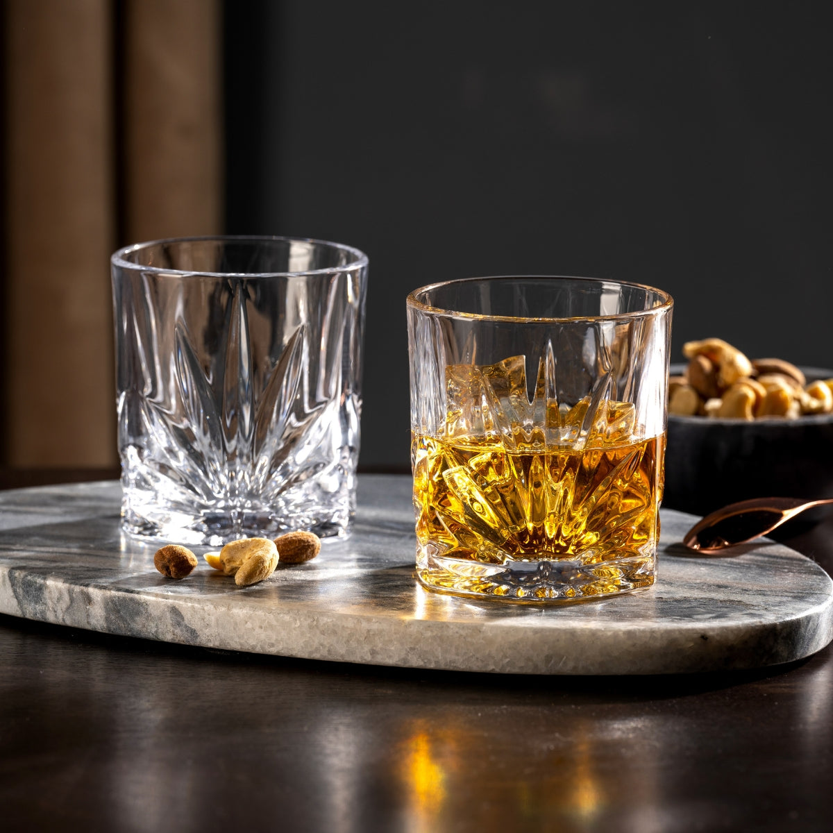 Zwei geschliffene Tumbler stehen auf einer edlen Marmorplatte, während goldener Whisky im Vordergrund funkelt