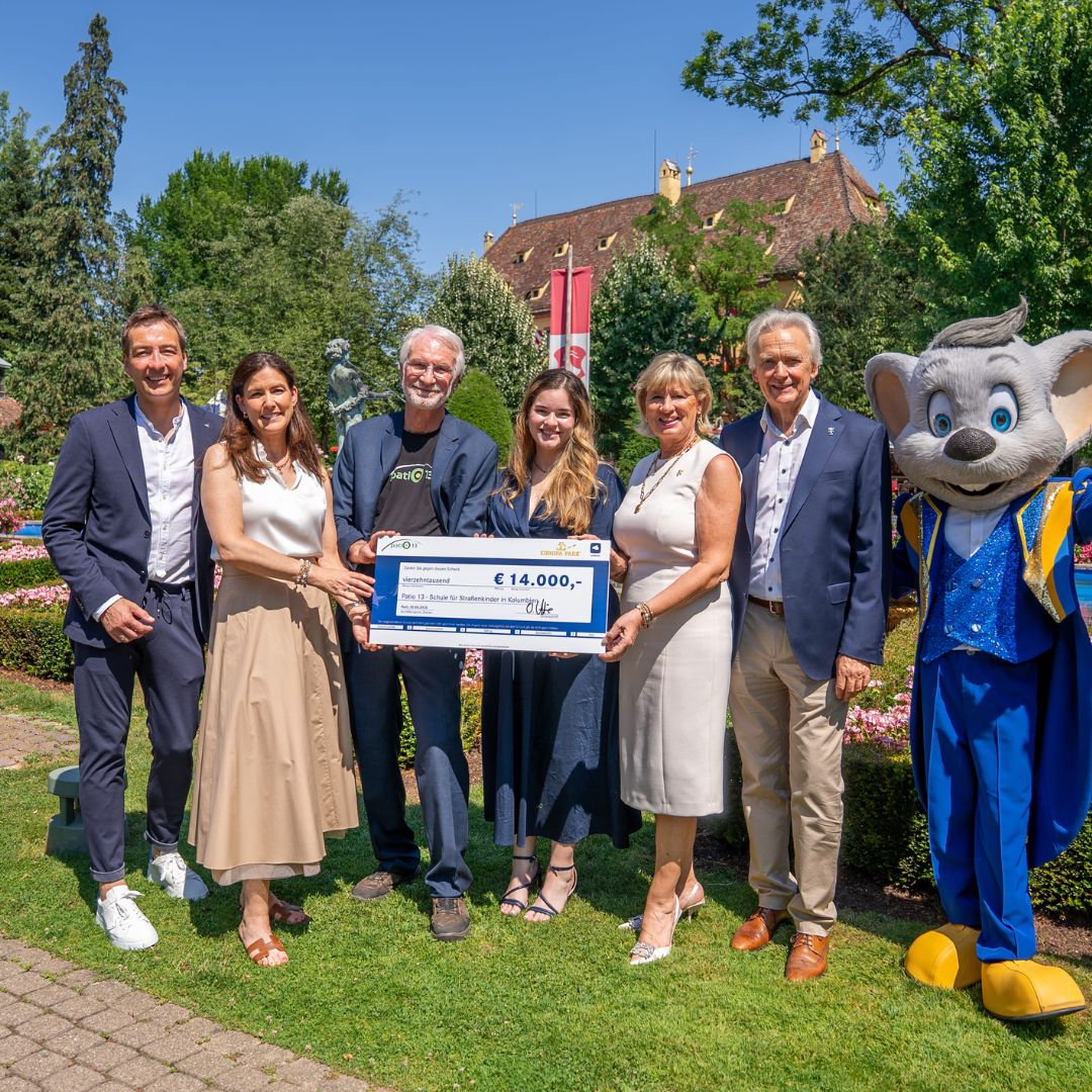Gruppenfoto bei der Spendenübergabe im Park – Vertreter:innen mit einem Scheck über 14.000 Euro, begleitet vom LEONARDO Maskottchen.