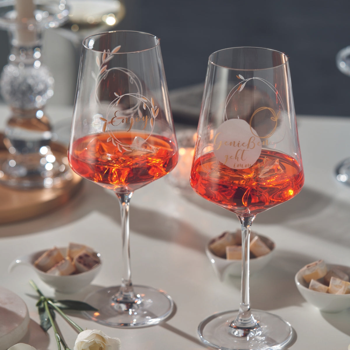 Zwei stilvolle Weingläser mit orangefarbenem Drink, filigraner Gravur und stimmungsvoller Tischdeko – ein Genussmoment im Kerzenschein.