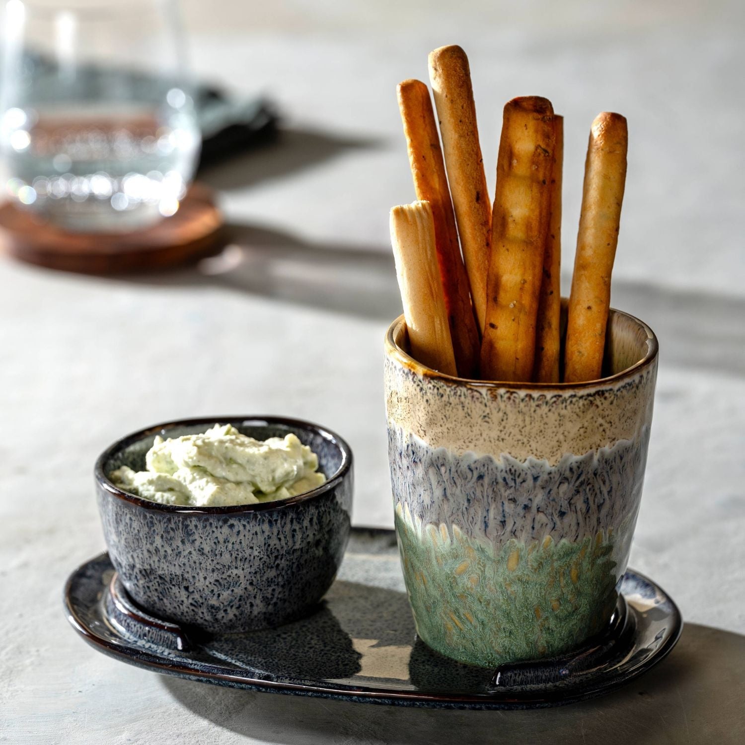 LEONARDO Keramikbecher mit knusprigen Grissini und passendem Schälchen mit cremigem Dip auf einem dunklen Servierteller.