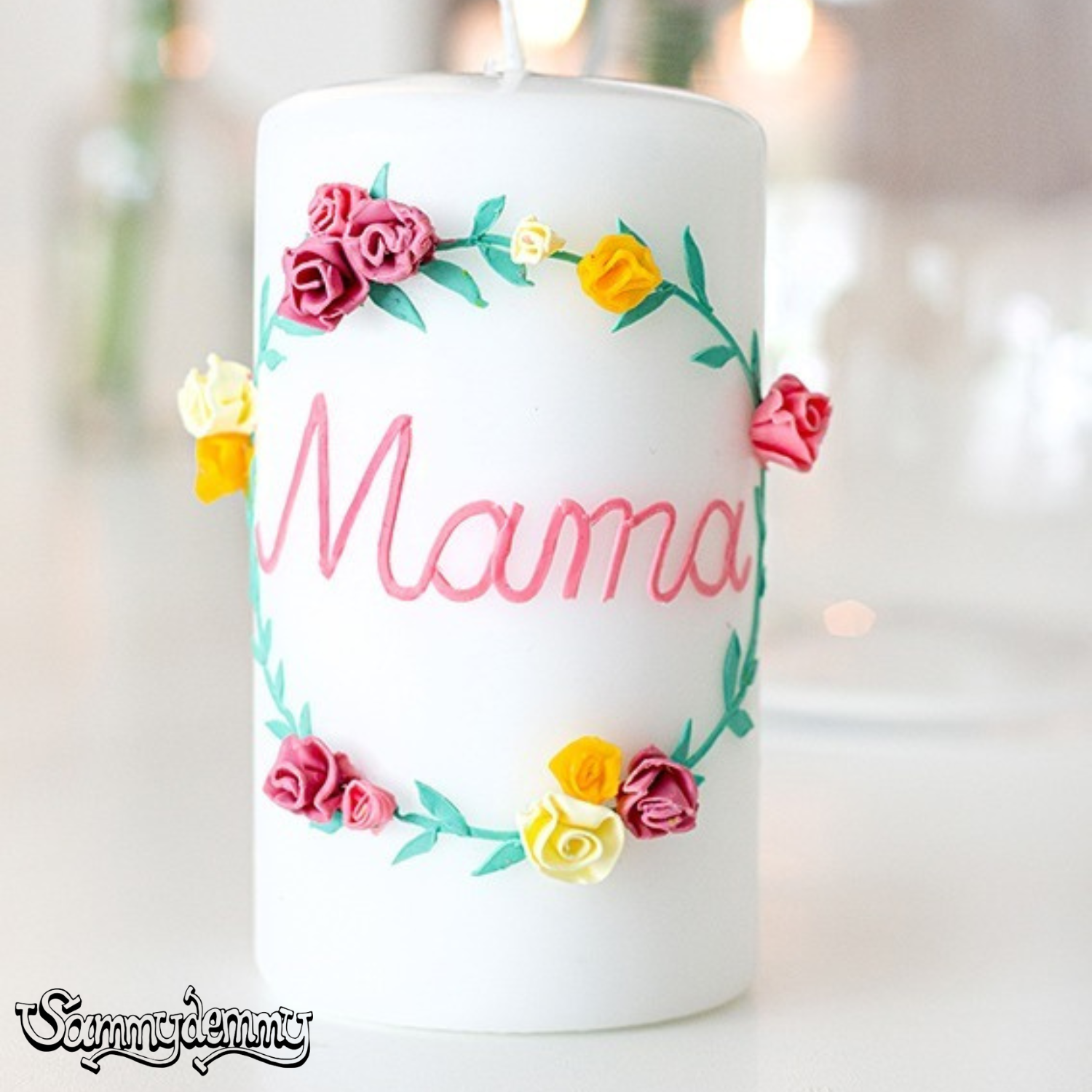 Weiße Kerze mit der Aufschrift „Mama“ in rosa Schrift und verziert mit kleinen Blüten in Rosa, Gelb und Creme – liebevoll gestaltetes Geschenk zum Muttertag.