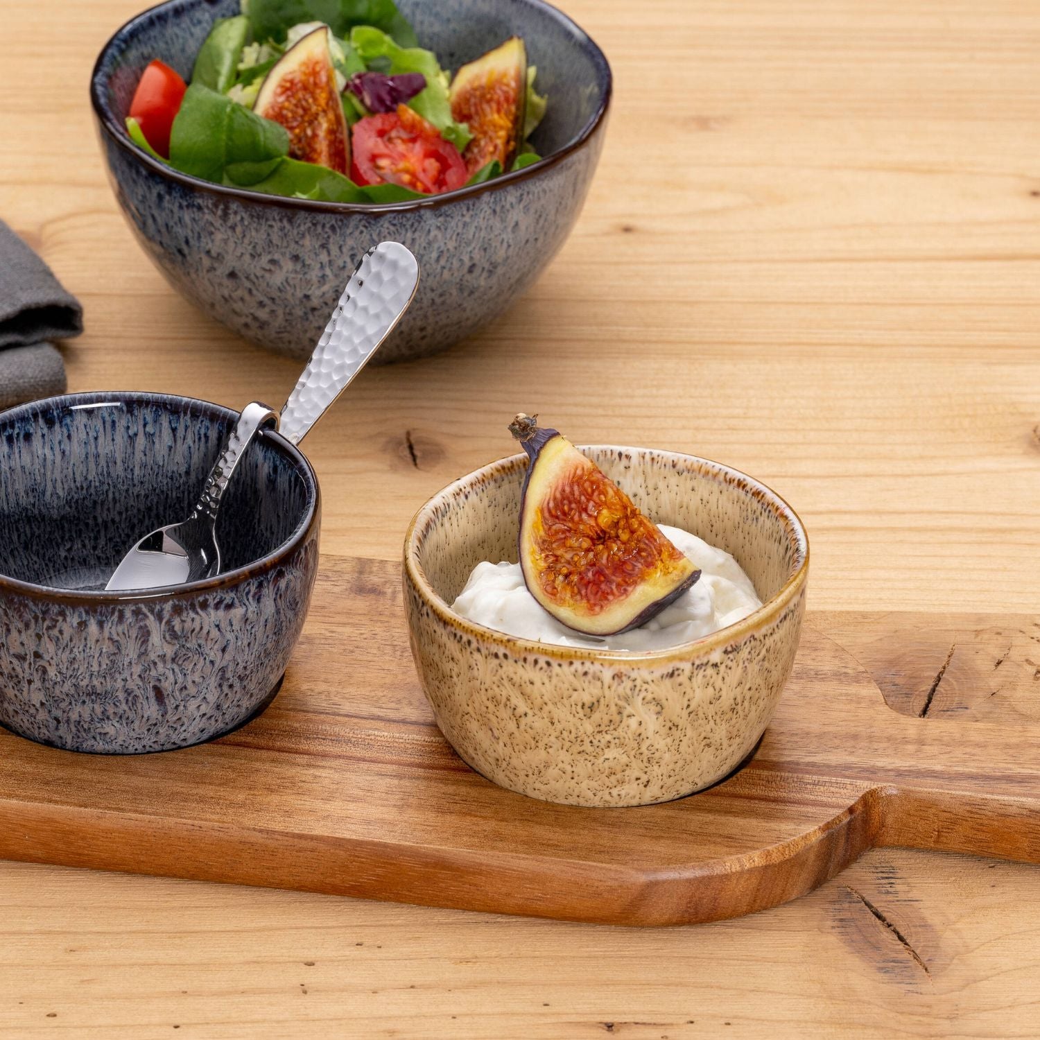 LEONARDO Keramikschälchen mit Dip und Feige auf Holzbrett, daneben zwei weitere Schalen mit Löffel und frischem Salat.
