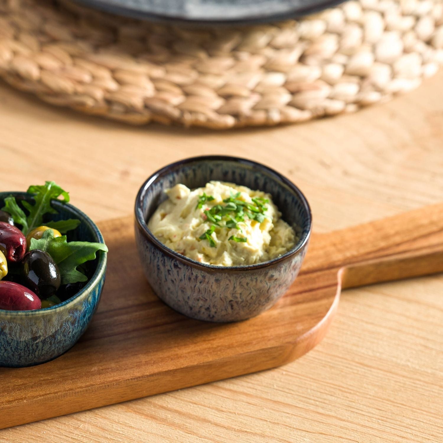 Zwei kleine, strukturierte Schalen aus Keramik von LEONARDO auf einem Holzbrett – eine gefüllt mit cremigem Dip, die andere mit mediterranem Salat.