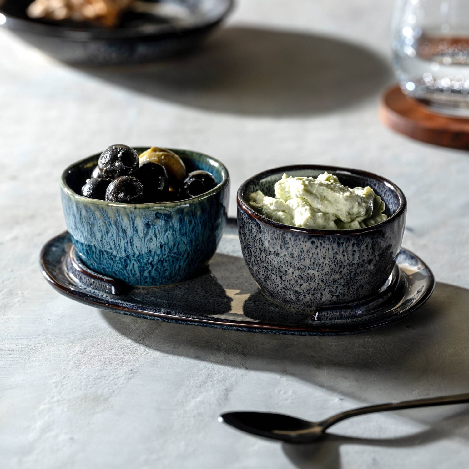 Zwei Keramikschälchen von LEONARDO auf passendem Teller – eines gefüllt mit schwarzen Oliven, das andere mit cremigem Dip.