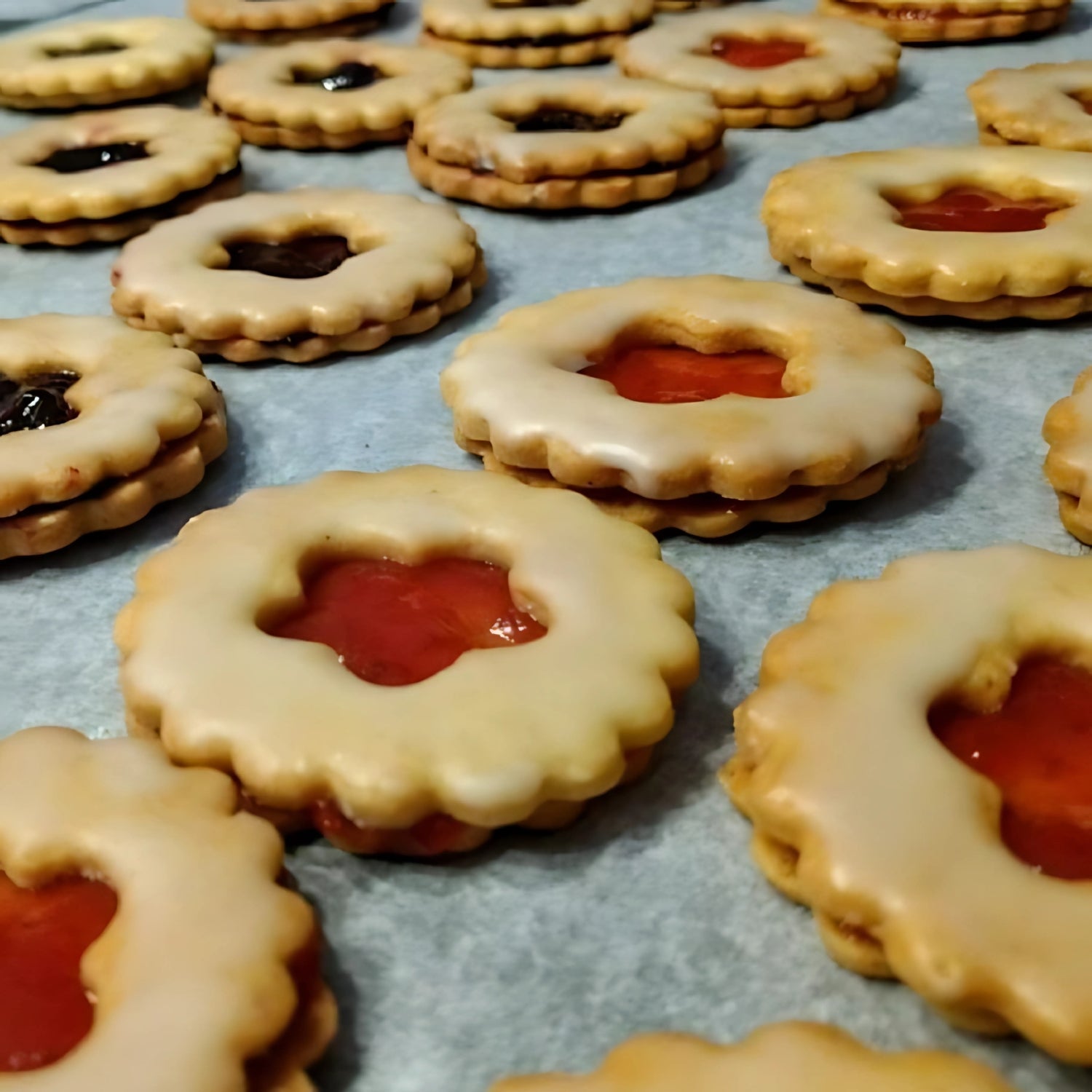 Gefüllte Doppelkekse mit Zuckerguss und roter oder dunkler Marmelade – frisch gebacken auf dem Blech.