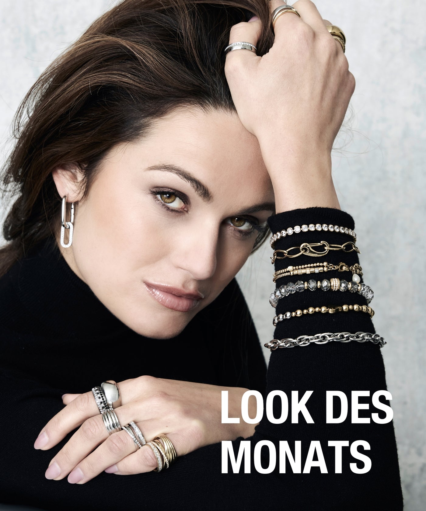 Eine Frau trägt auffällige silberne Ringe und filigrane Armbänder in Gold und Schwarz, während sie sich lässig auf ihren Arm stützt – daneben steht der Schriftzug „LOOK DES MONATS“.