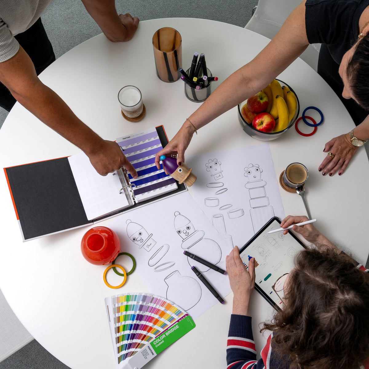 Team bei der kreativen Produktentwicklung am Tisch mit Skizzen, Farbmusterfächern und digitalen Entwürfen.