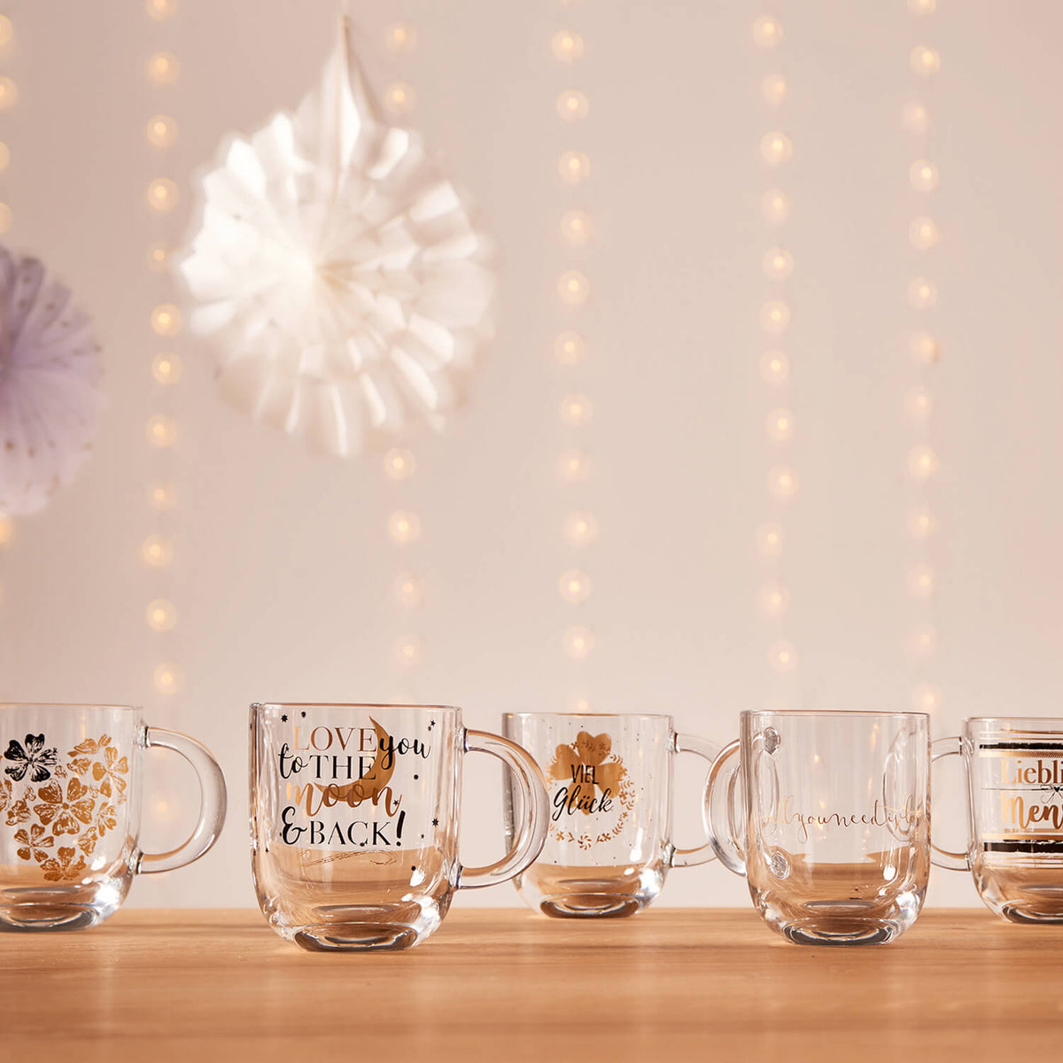 Mehrere Glastassen mit verschiedenen Motiven auf Holztisch, dekorativ arrangiert