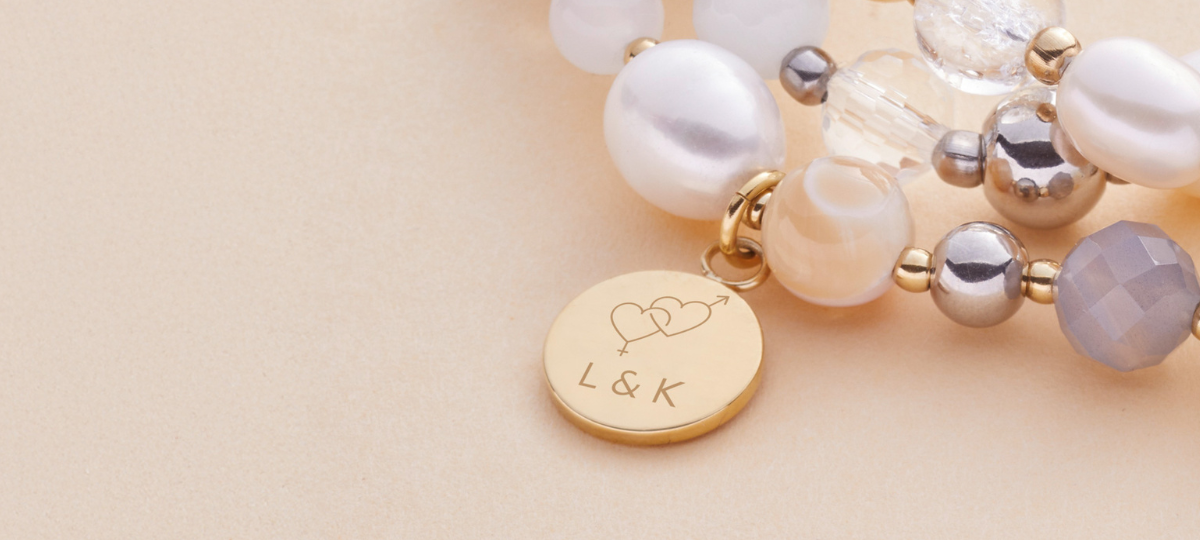 Armband HOPE mit Gravur. "L & K" steht dadrauf sowie ein Symbol, welches zwei ineinander verschlungene Herzen zeigt sowie das Zeichen für Männlich und Weiblich