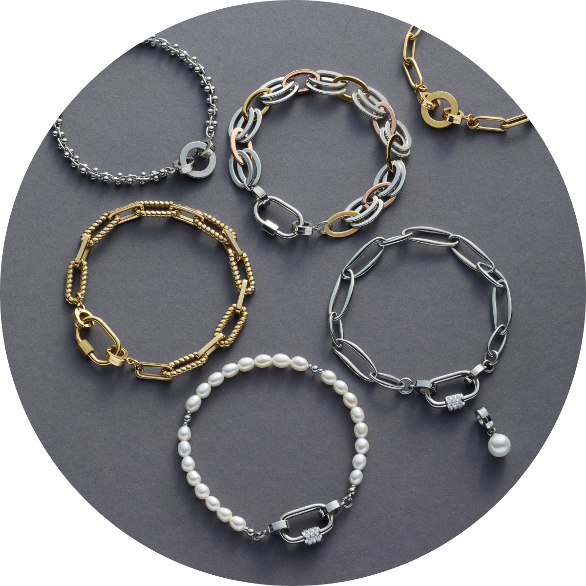 Sechs trendige Armbänder in Gold, Silber und mit Perlen, mit markanten Gliedern oder Karabinerverschlüssen auf grauem Untergrund.