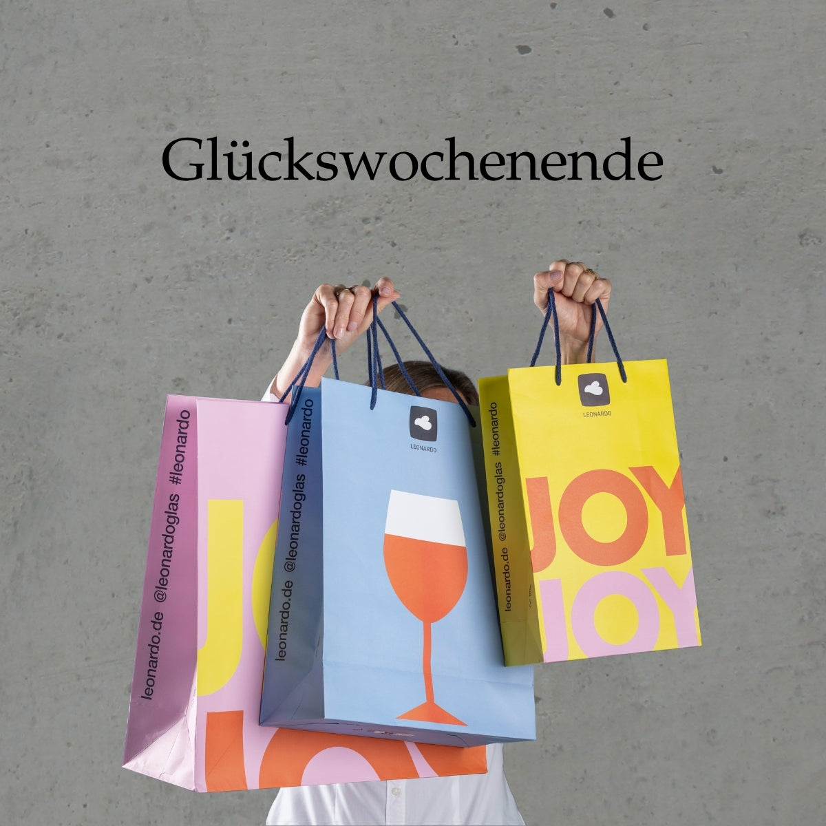 Glückswochenende: Hände halten bunte Papiertüten mit Weinglasdesign in Rosa, Blau und Gelb