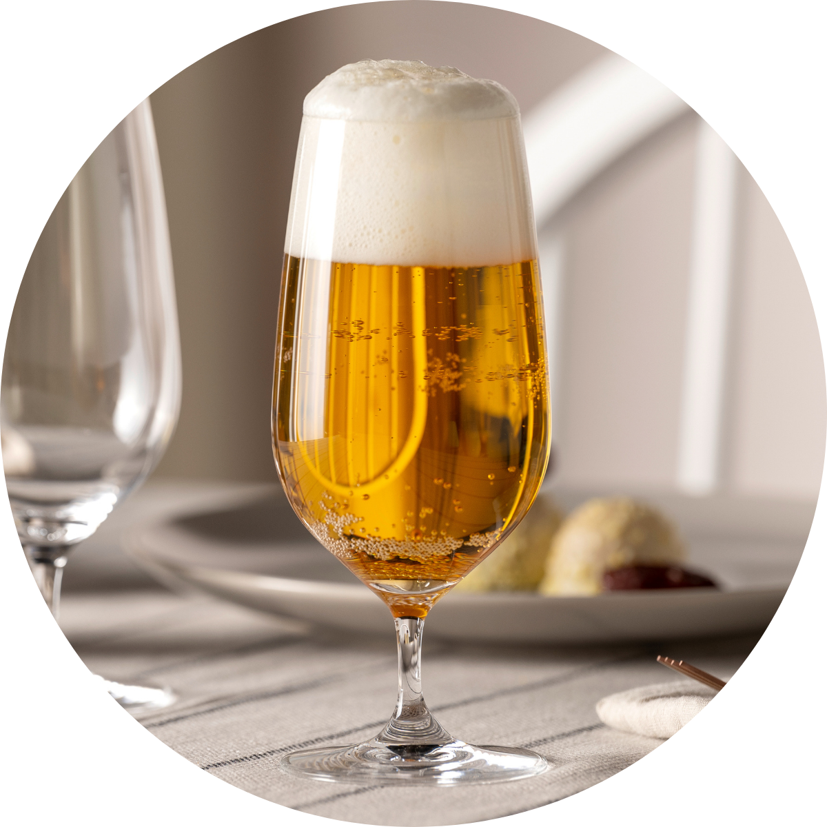 Goldenes, sprudelndes Bier mit fester Schaumkrone in einem feinen Bierglas auf gedecktem Tisch.