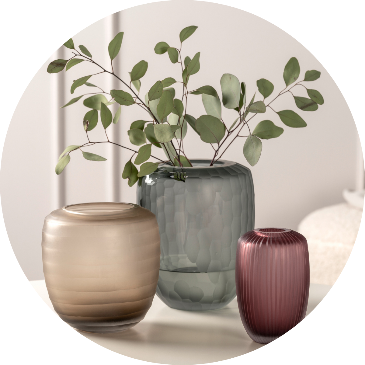 Drei unterschiedlich große Vasen in Beige, Grau und Aubergine mit Eukalyptuszweig dekoriert.