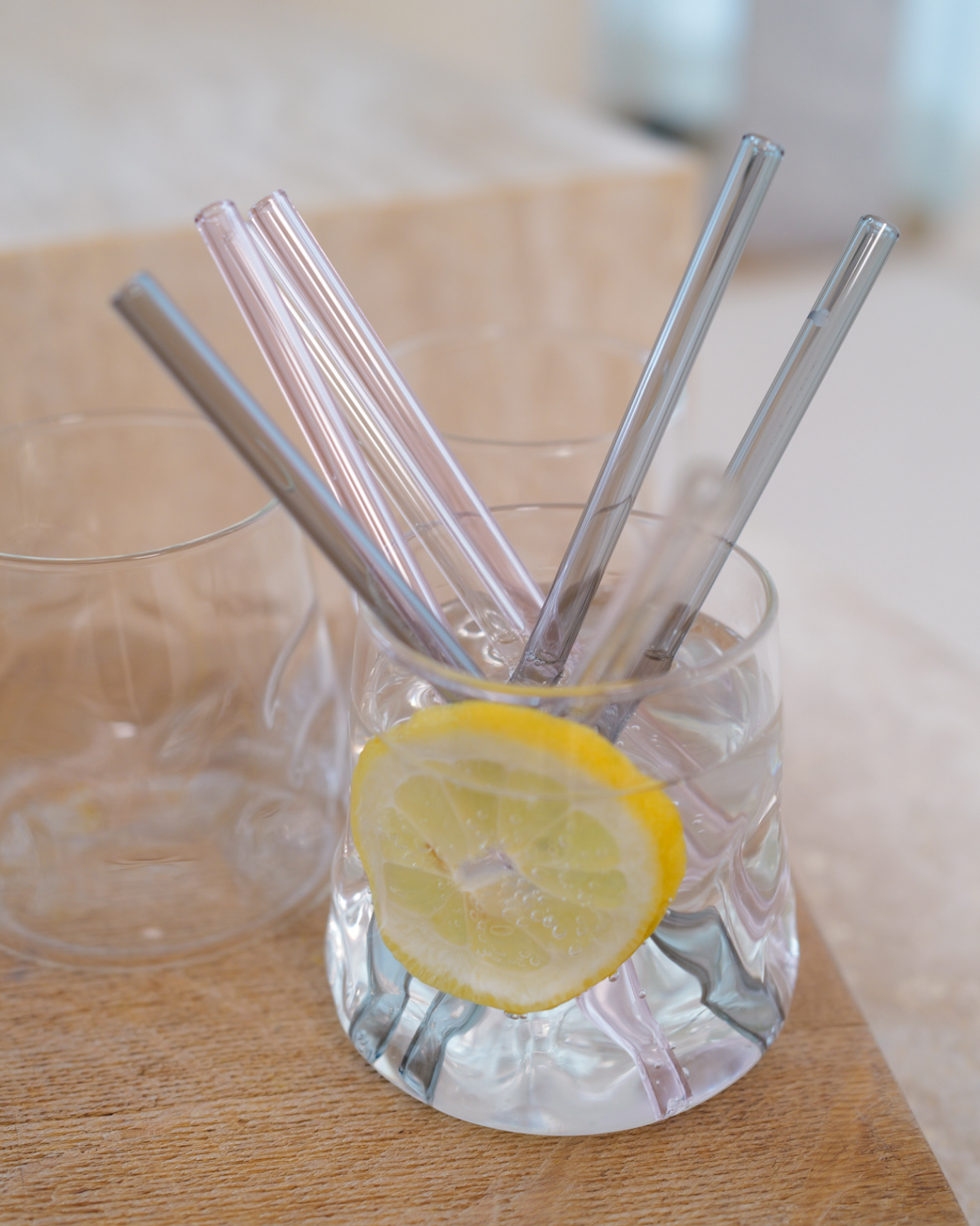 Mehrere Glasstrohhalme in verschiedenen Farben stehen in einem Glas mit Zitronenscheibe.