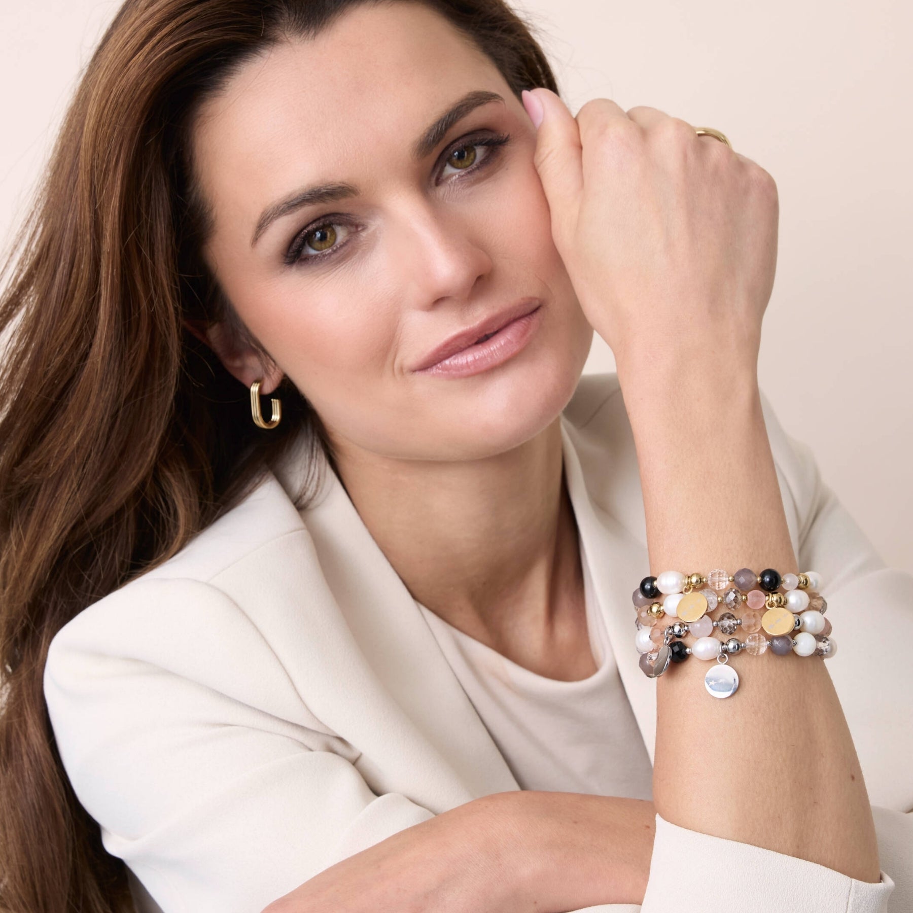 Eine Frau trägt mehrere farbenfrohe Armbänder mit goldenen und perligen Details am Handgelenk – stilvoll kombiniert mit einem hellen Blazer und dezentem Make-up.