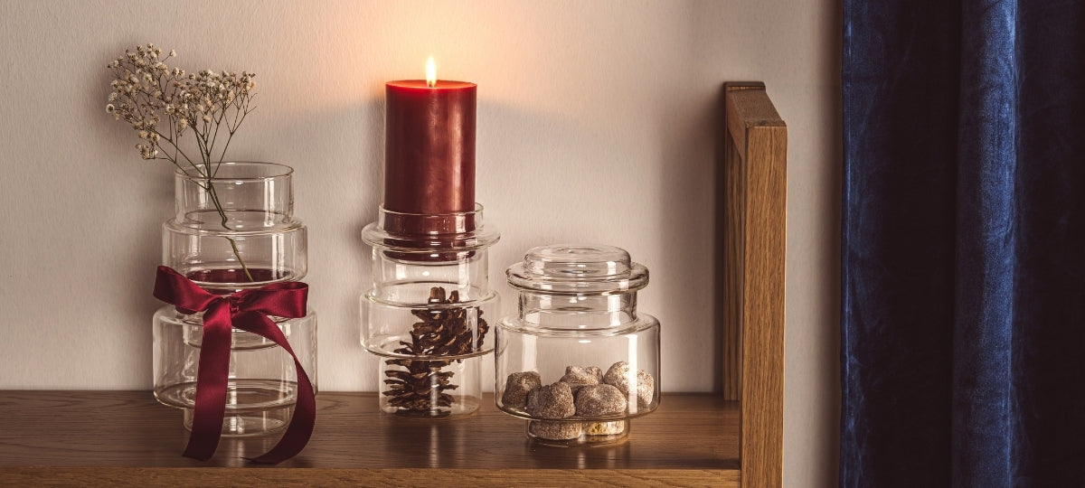 Weihnachtliche Dekoration mit roter Kerze, Glaszylinder mit Trockenblumen und roten Schleife, Tannenzapfen und goldenem Schmuck