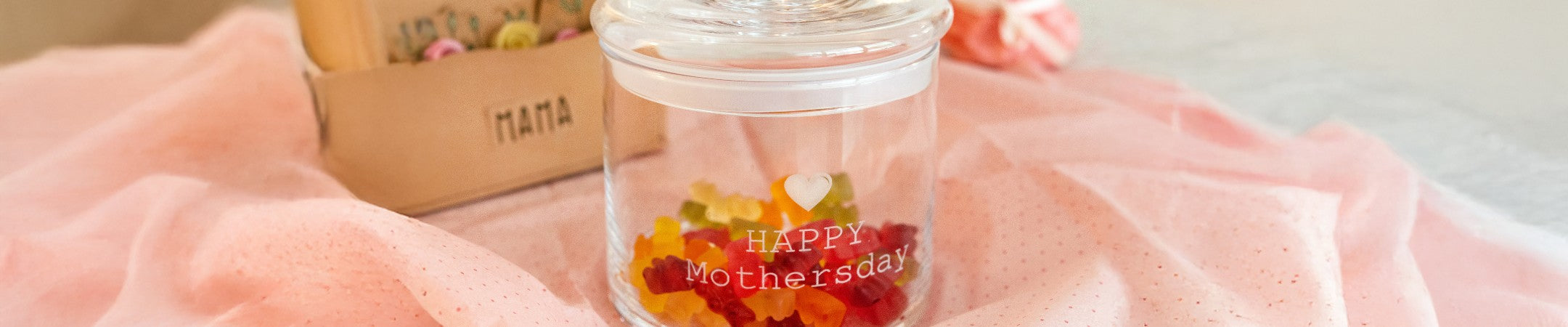 LEONARDO Glasdose TOP mit Gravur „HAPPY Mothersday“, gefüllt mit Gummibärchen, dekorativ inszeniert mit Muttertagsgeschenk im Hintergrund.