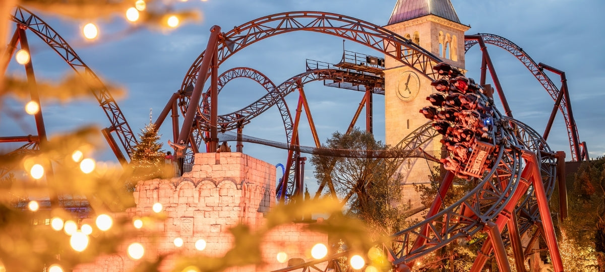 Atemberaubende Achterbahn im Europa-Park bei Abenddämmerung, festlich beleuchtet mit warmer Weihnachtsbeleuchtung und Blick auf den Uhrturm im Hintergrund.