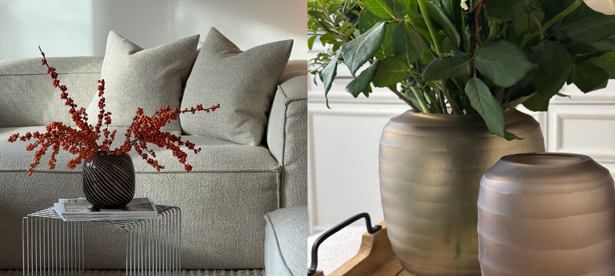 Wohnszene mit grauem Sofa und Vase mit roten Beerenzweigen, daneben Weißweingläser mit Flasche sowie zwei matte Dekovasen mit grüner Pflanze.