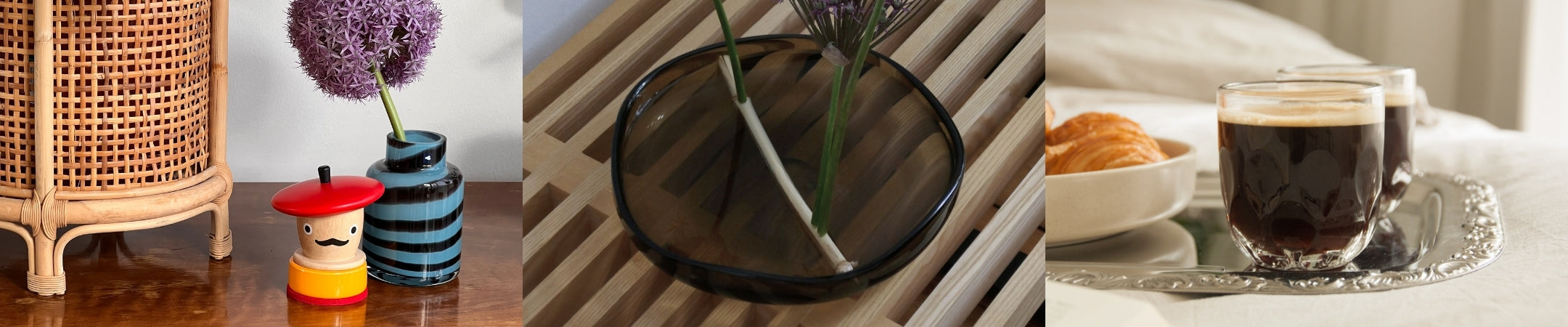 Dekorative Objekte und Geschenkideen: Rattanlampe, rote Kerze, gestreifte Vase mit lila Blüten, schwarze Schale mit Pflanze, Kaffee und Croissant auf Tablett