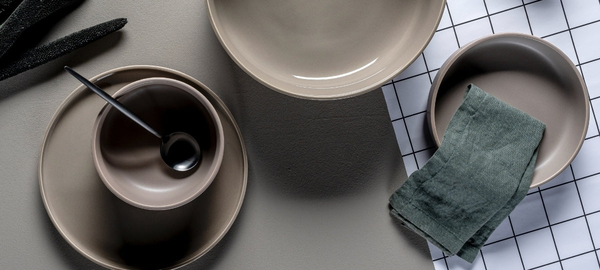 Elegantes Geschirr Set in Grautönen mit Tellern, Schale und grünem Leinentuch auf minimalistischem Hintergrund