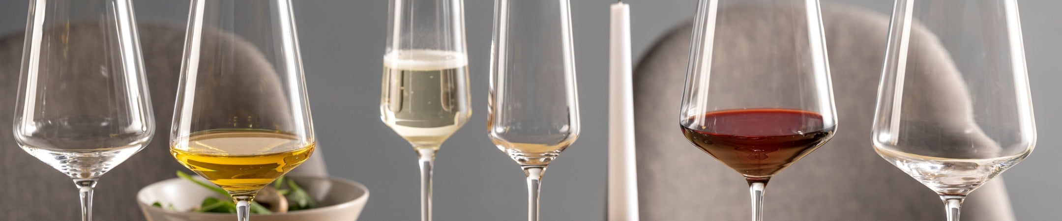 Sechs elegante Weingläser in einer Reihe mit verschiedenen Füllungen: Weißwein, Rosé, Rotwein und leere Gläser vor grauem Hintergrund