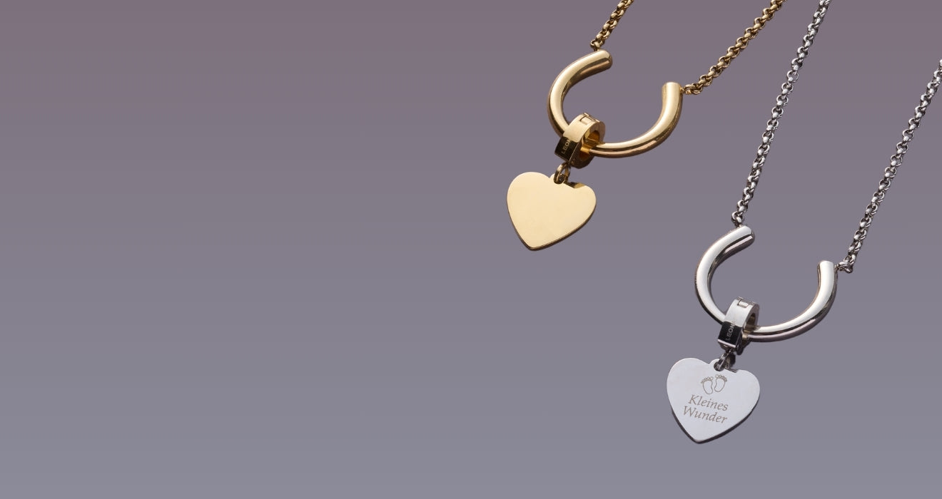 Zwei Halsketten mit gravierbaren Herz-Anhängern in Gold und Silber aus der Gravur-Kollektion, freigestellt vor einem lila Hintergrund.