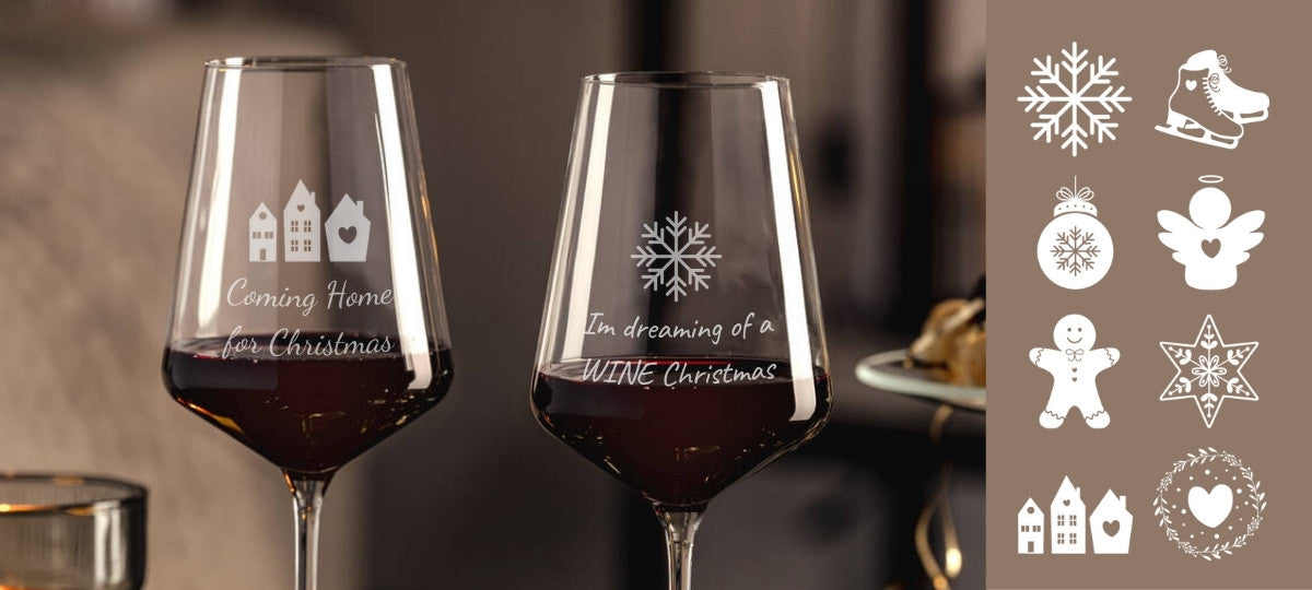 Zwei Weingläser mit Gravuren in weihnachtlichem Stil. Auf dem linken Glas steht „Coming Home for Christmas“ mit kleinen Häusern, auf dem rechten eine Schneeflocke mit dem Text „I’m dreaming of a WINE Christmas“. Daneben sind weiße winterliche Gravursymbole wie Schneeflocke, Engel, Lebkuchenmann und Stern auf braunem Hintergrund dargestellt.