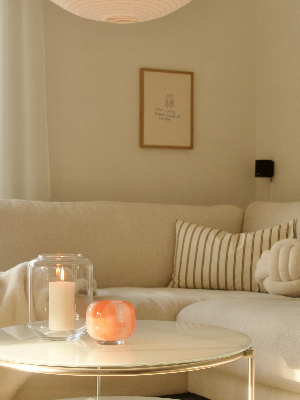 Helles Wohnzimmer mit beigem Ecksofa, gestreiftem Kissen und rundem Couchtisch mit Glaswindlicht und Kerze.