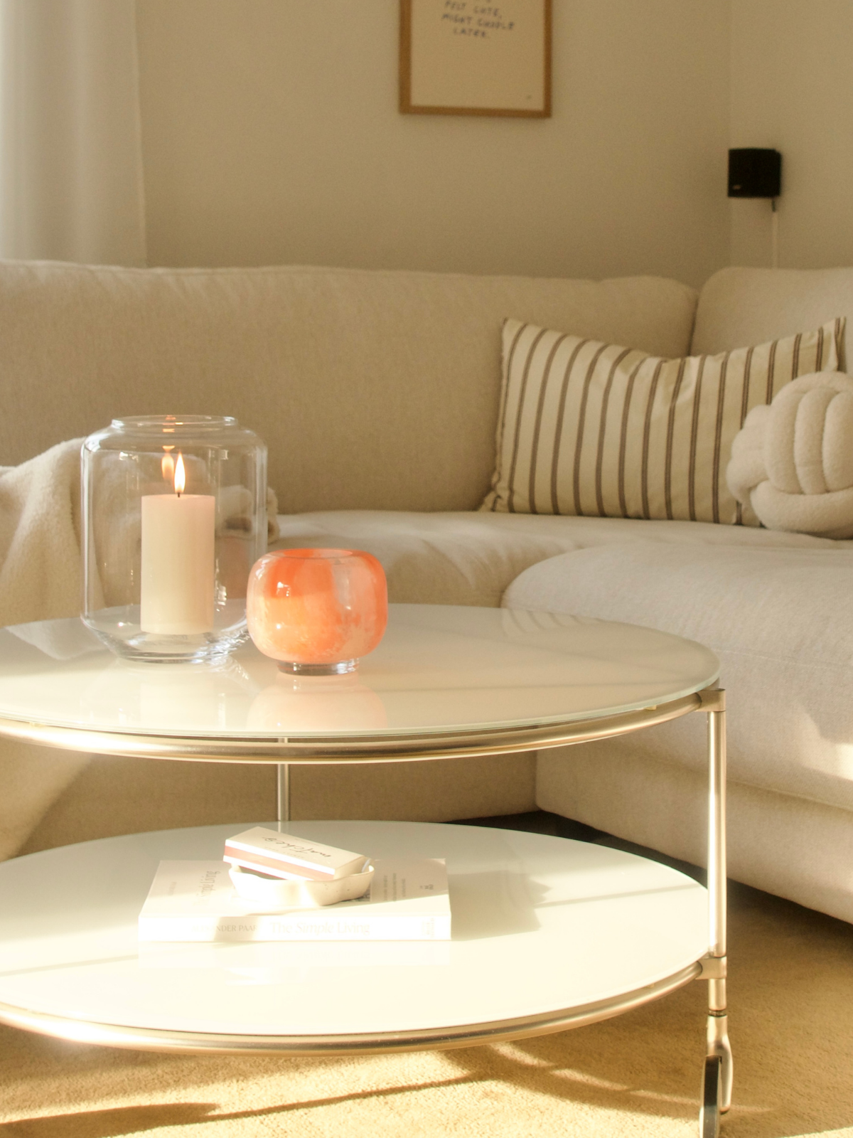 Helles Wohnzimmer mit Ecksofa, Couchtisch und brennender Kerze im Glas; an der Wand hängt ein gerahmtes Bild.