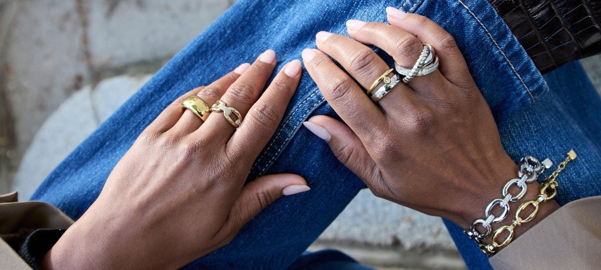 Zwei Personen mit eleganten silbernen und goldenen Ringen an den Händen auf blauer Jeanshose sitzend