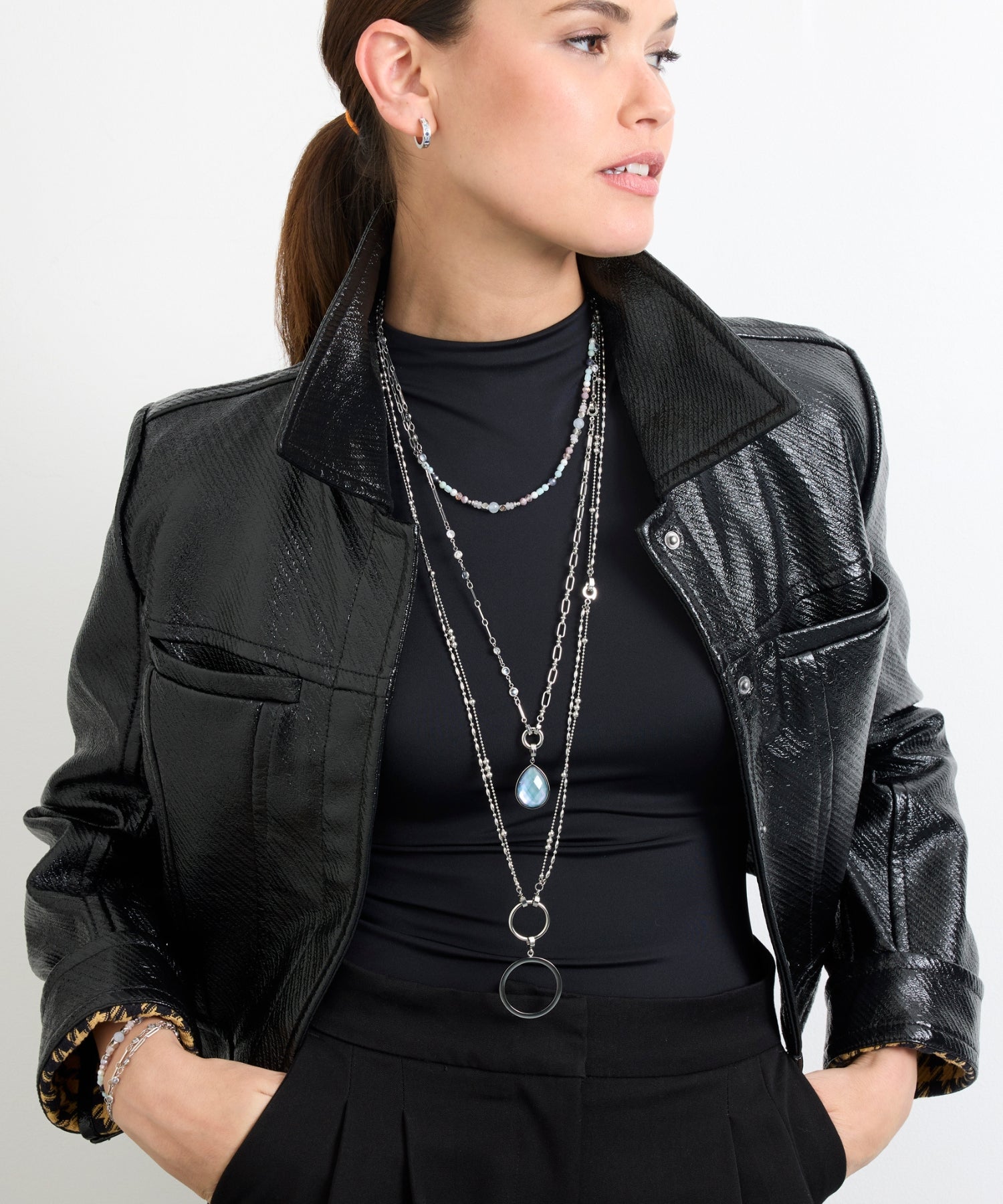 Frau in schwarzer Jacke trägt mehrlagige LEONARDO-Ketten mit Perlen und blauem Anhänger