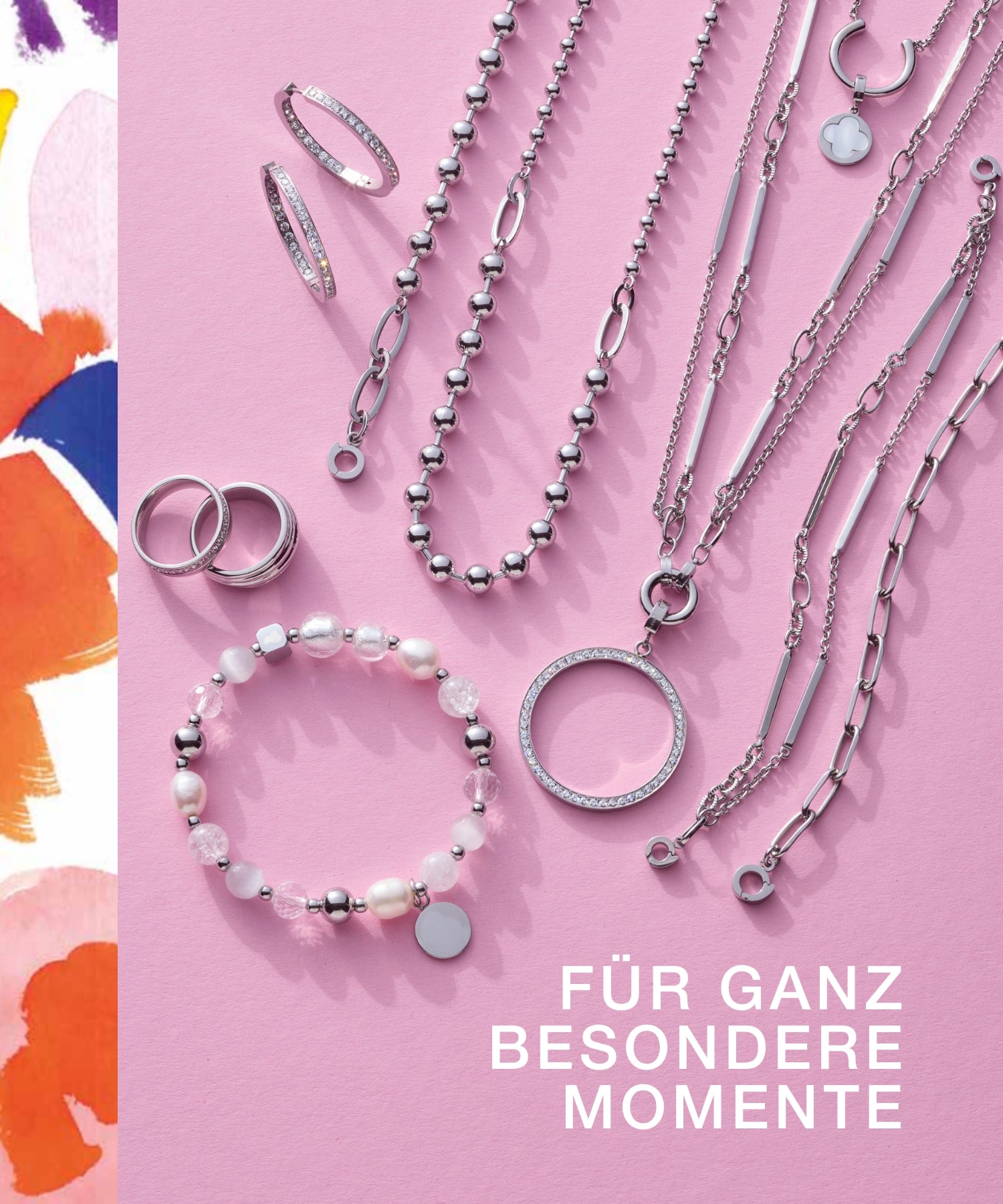 Flach gelegter Schmuck auf rosa Hintergrund: silberne Ketten mit Anhängern, Armbänder mit Perlen, Ringe und Creolen. Links ein farbiger Rand, daneben der Text "FÜR GANZ BESONDERE MOMENTE".