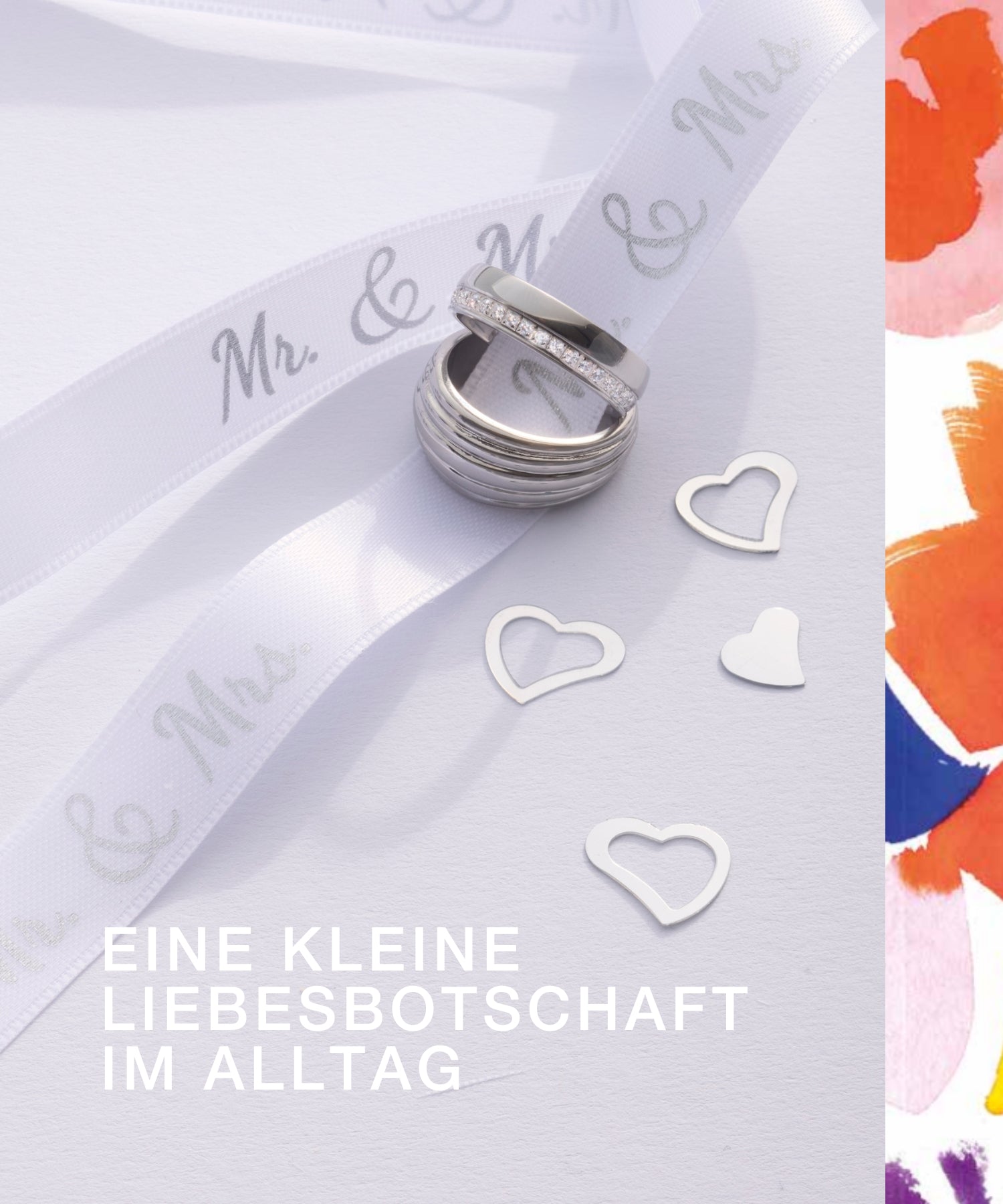 Silberne Ringe auf weißem Hintergrund mit Mr. & Mrs.-Geschenkband und ausgestanzten weißen Herzen. Der Text „EINE KLEINE LIEBESBOTSCHAFT IM ALLTAG“ ist unten rechts platziert.