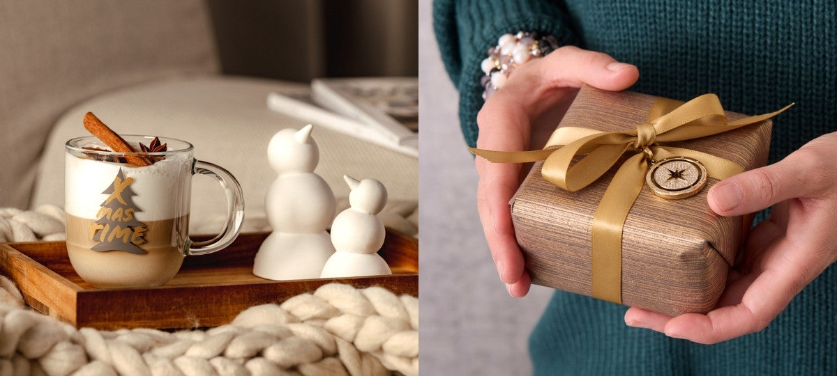 Eine gemütliche weihnachtliche Szene: links steht auf einem Holztablett eine Tasse Latte Macchiato mit Zimtstange und der Aufschrift „XMAS TIME“, daneben zwei kleine weiße Schneemannfiguren. Rechts hält eine Person in einem grünen Strickpullover ein Geschenk mit goldener Schleife und rundem Anhänger.