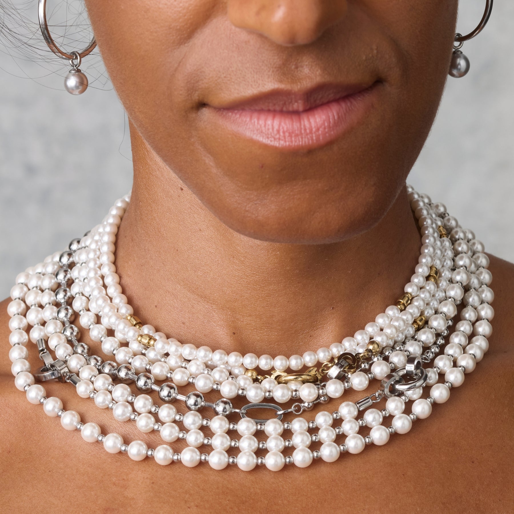 Mehrreihige Perlenketten in Weiß mit silbernen und goldfarbenen Details schmücken den Hals einer Frau – edel, opulent und modern interpretiert.