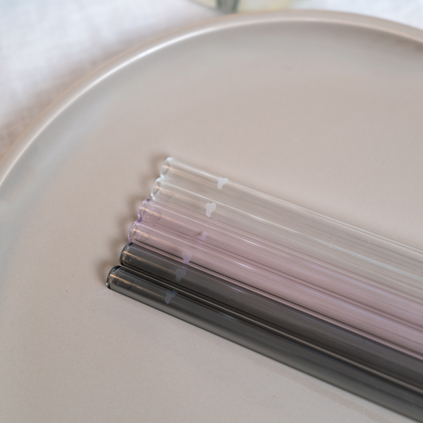 Mehrere wiederverwendbare Glasstrohhalme in transparent, rosa und grau auf hellem Untergrund.