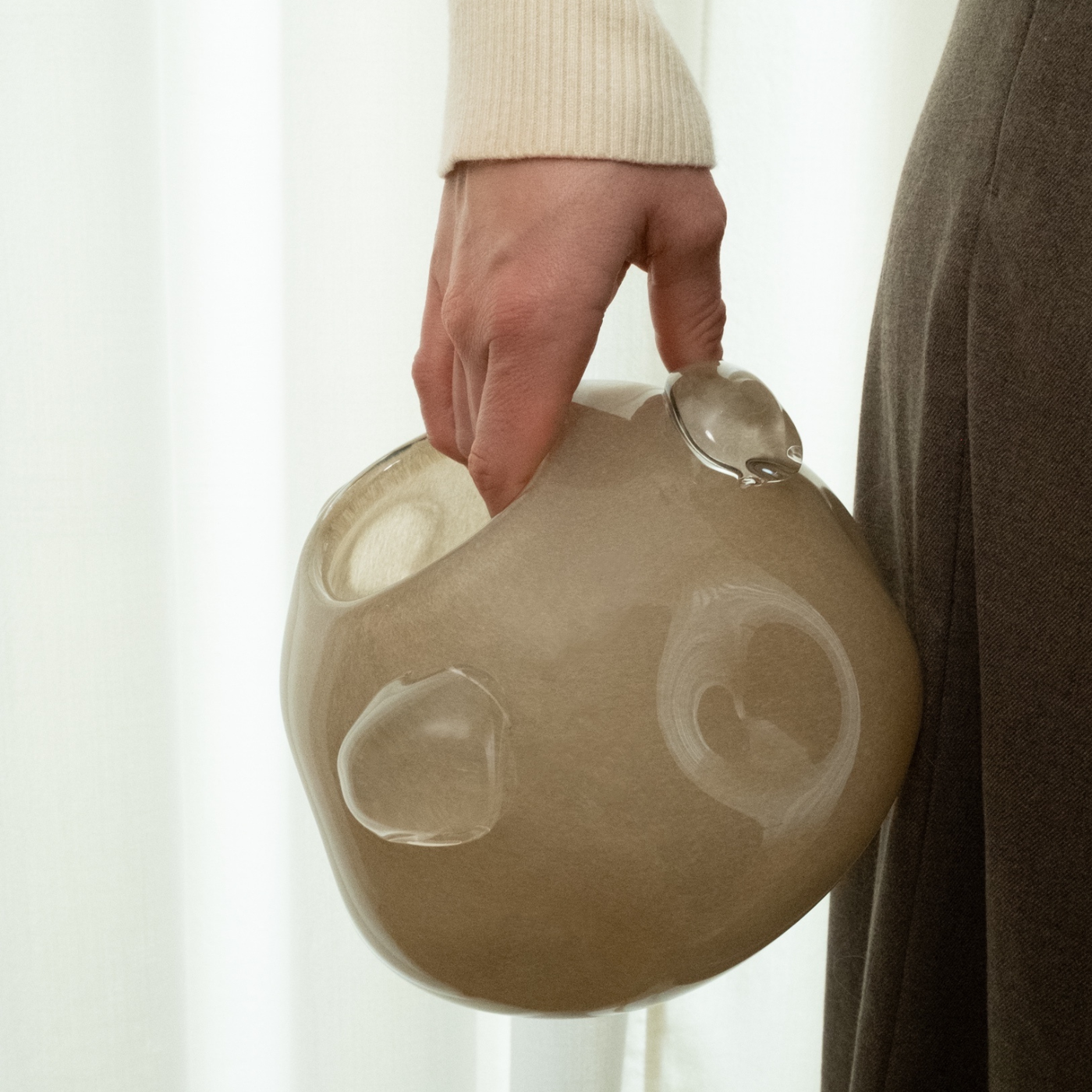 Beige Glasvase mit runden Glaselementen, seitlich von einer Person gehalten.