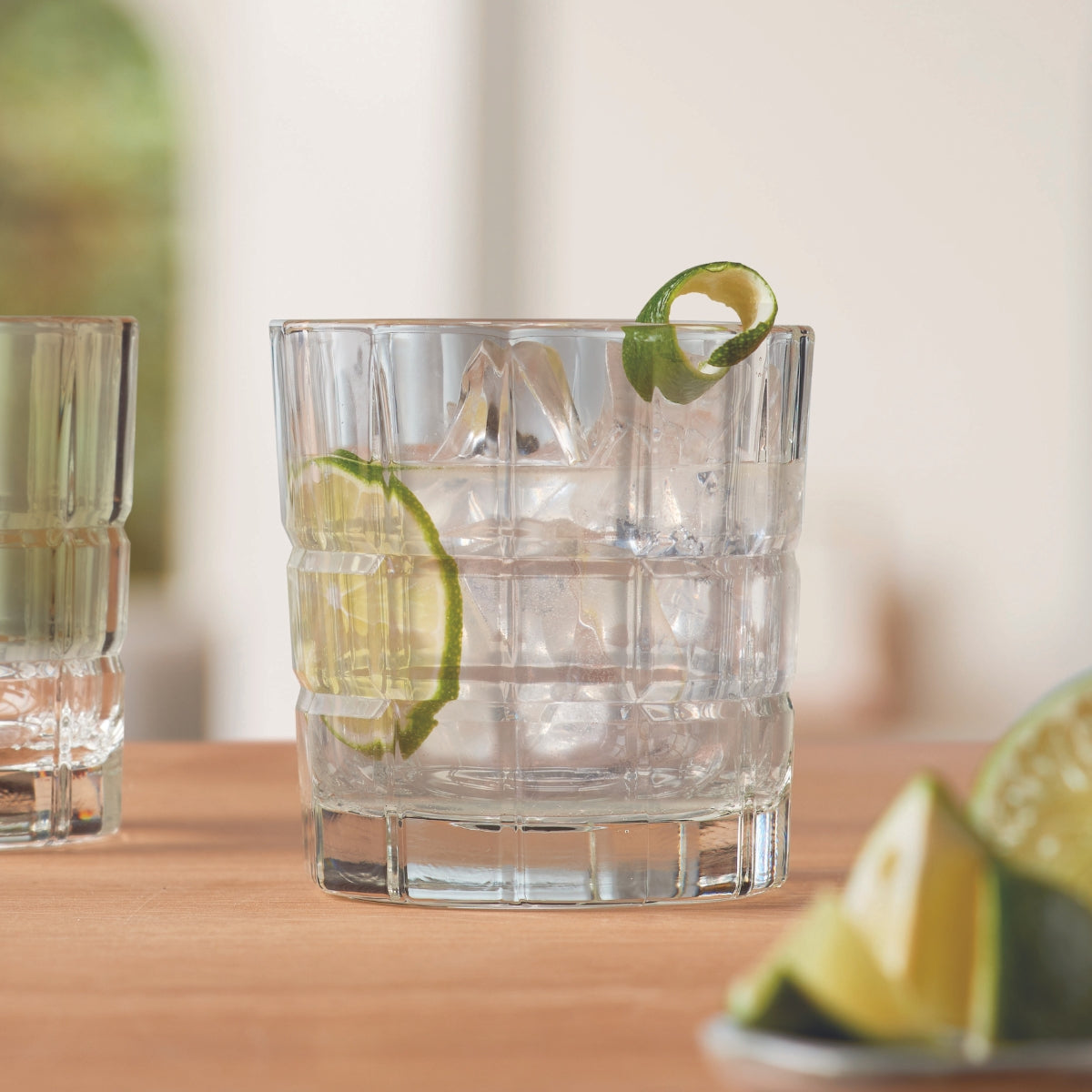 Ein klarer Drink mit Eiswürfeln und Limettenscheibe in einem strukturierten Glas.