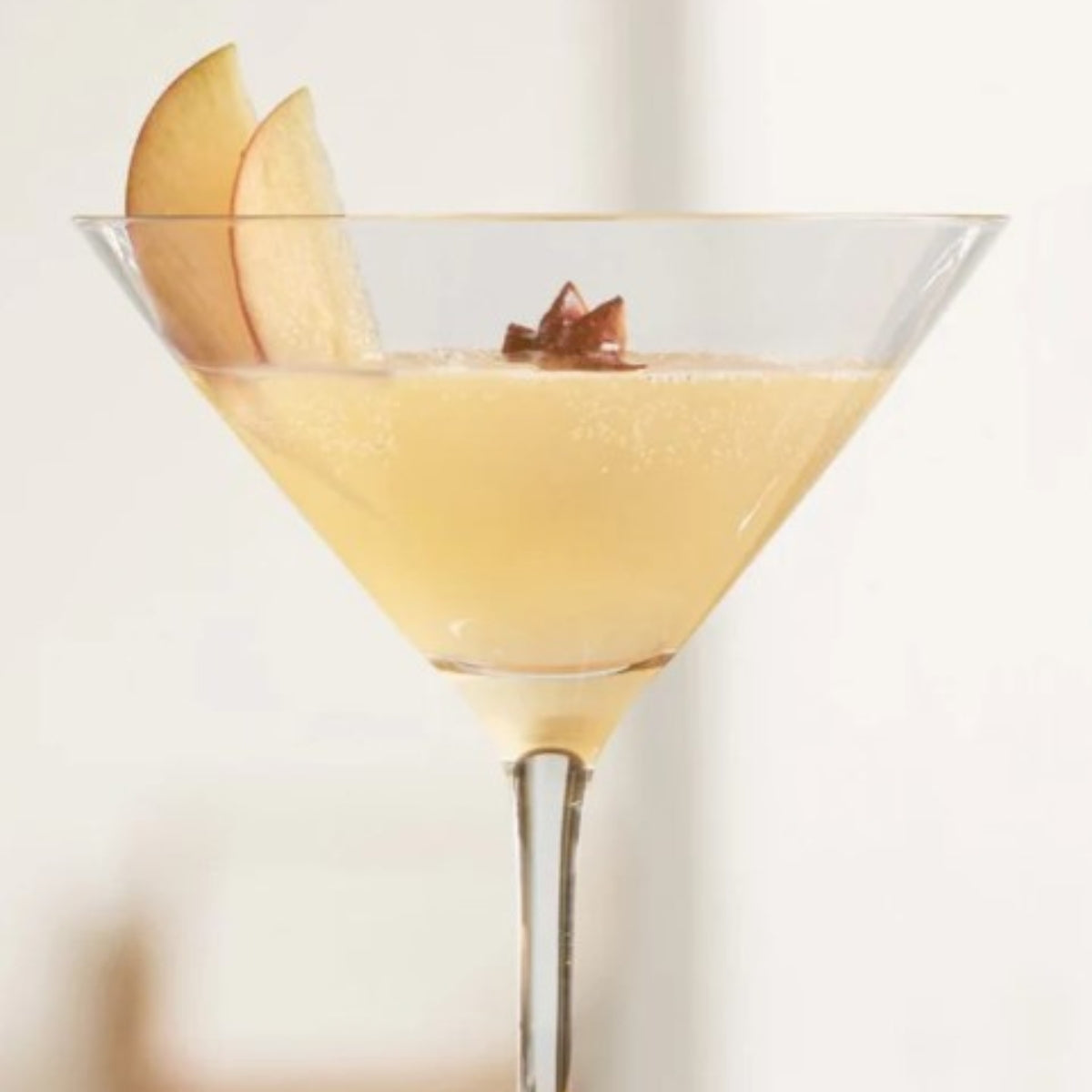 Ein heller Drink im Martiniglas, garniert mit Apfelscheiben und Sternanis.