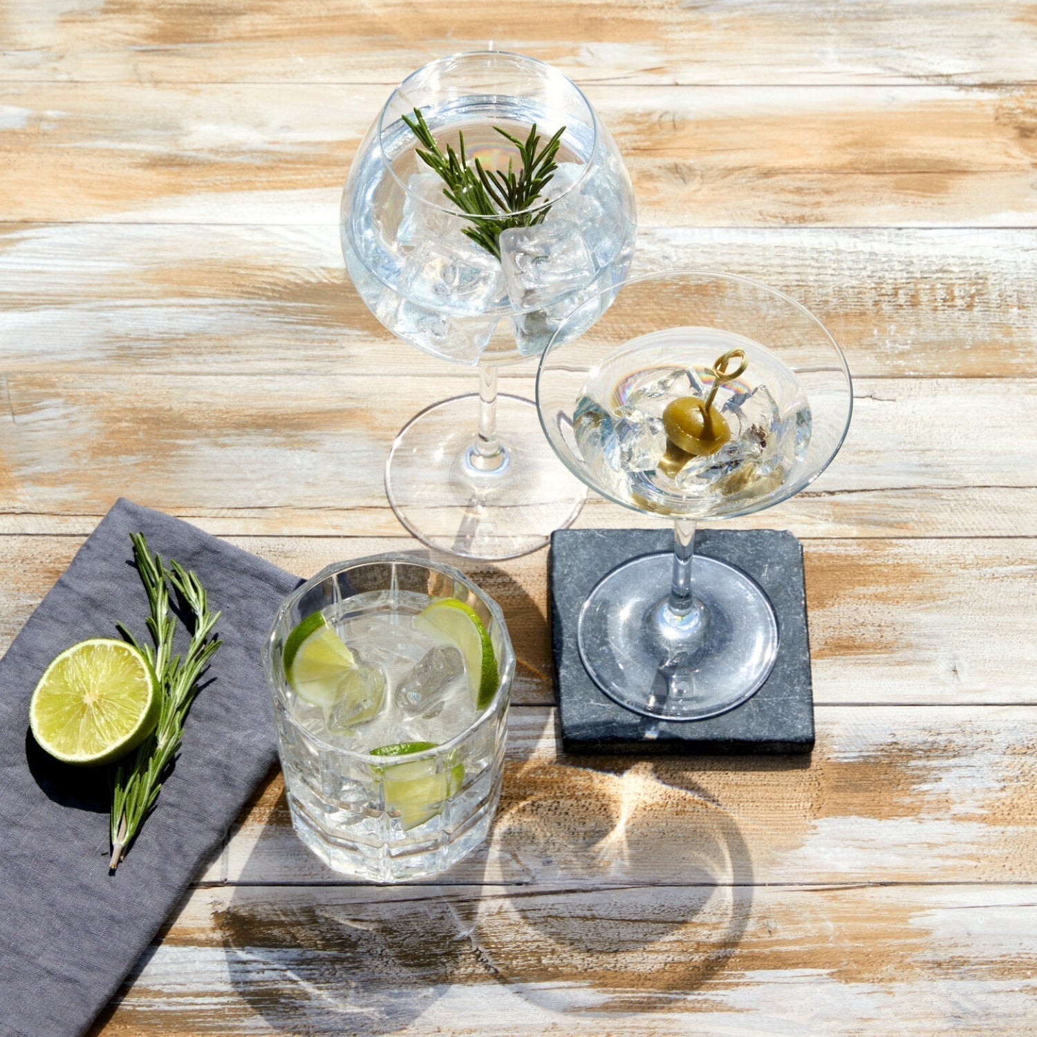 Drei LEONARDO Cocktailgläser mit Eis und Deko, auf einem Holztisch arrangiert.