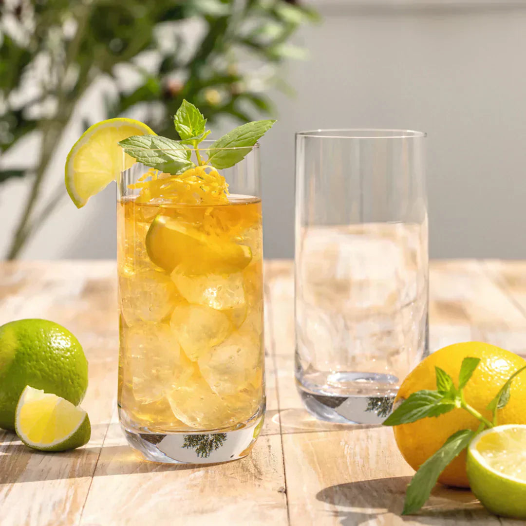 Ein Longdrinkglas mit Eistee, Limetten, Zitronenzeste und frischer Minze.