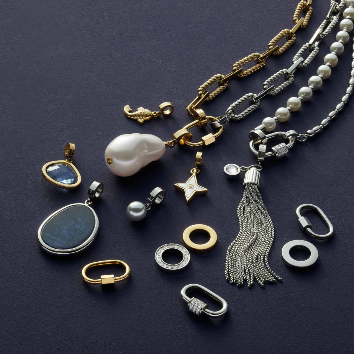 Schmuckkollektion mit goldenem Anhänger WILMA, Ketten, Ringen und Perlendetails auf grauem Hintergrund