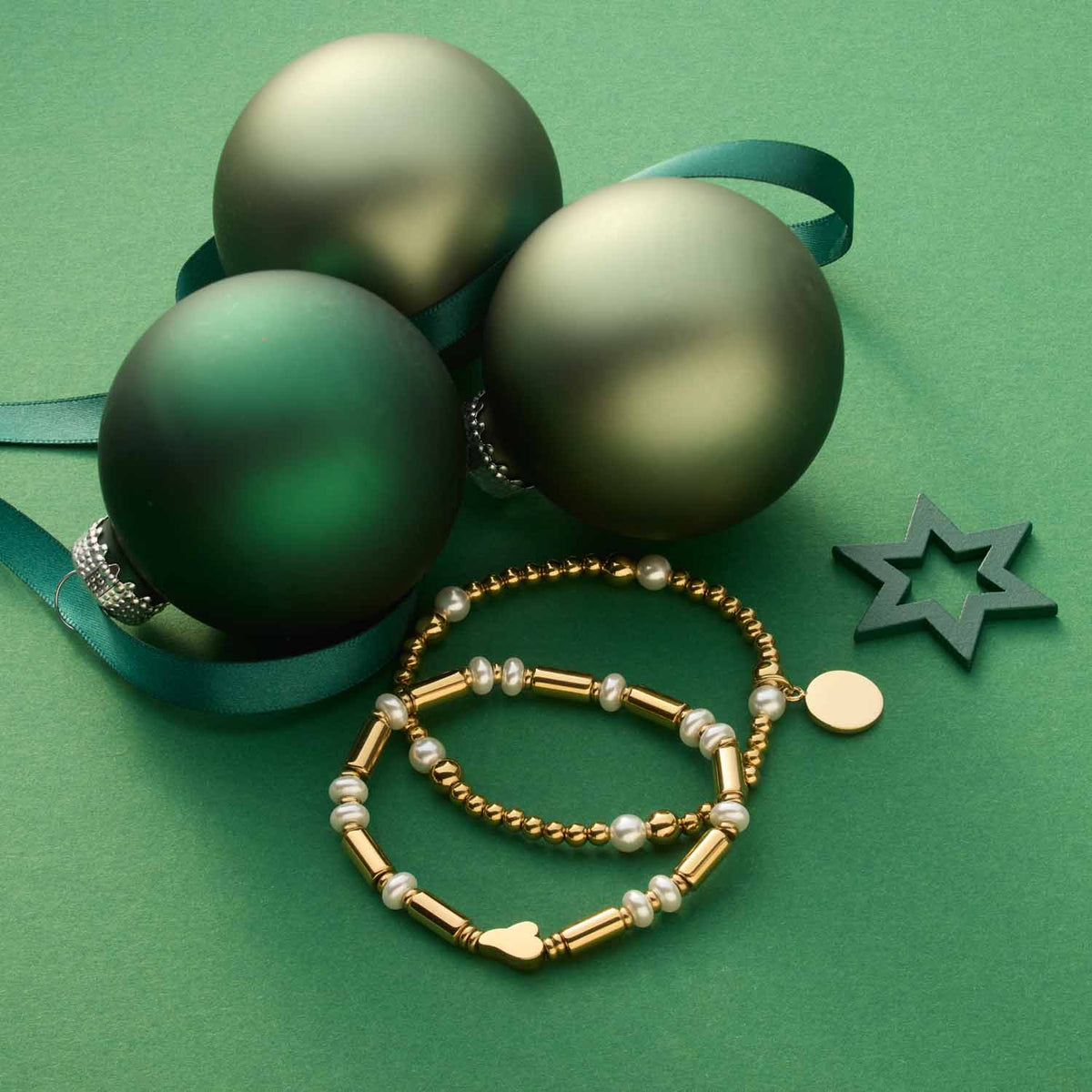 Armband NINA gold mit grünen Weihnachtskugeln und Dekoelementen auf grünem Hintergrund