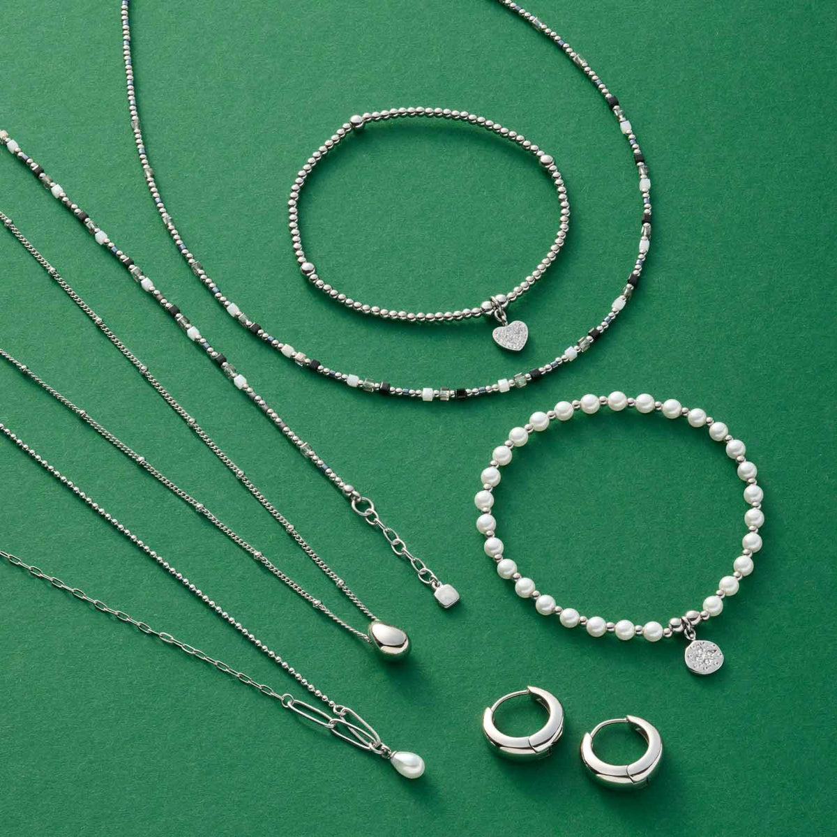 Silberne Armbänder, Ketten und Ohrringe auf grünem Hintergrund arrangiert