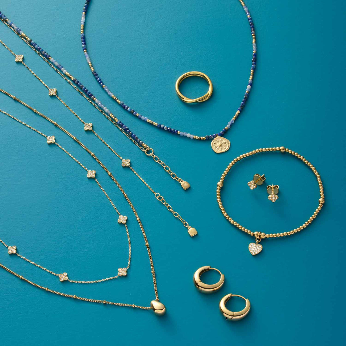 Goldene Schmuckkollektion auf türkisblauem Hintergrund mit Ketten, Ringen und Ohrringen