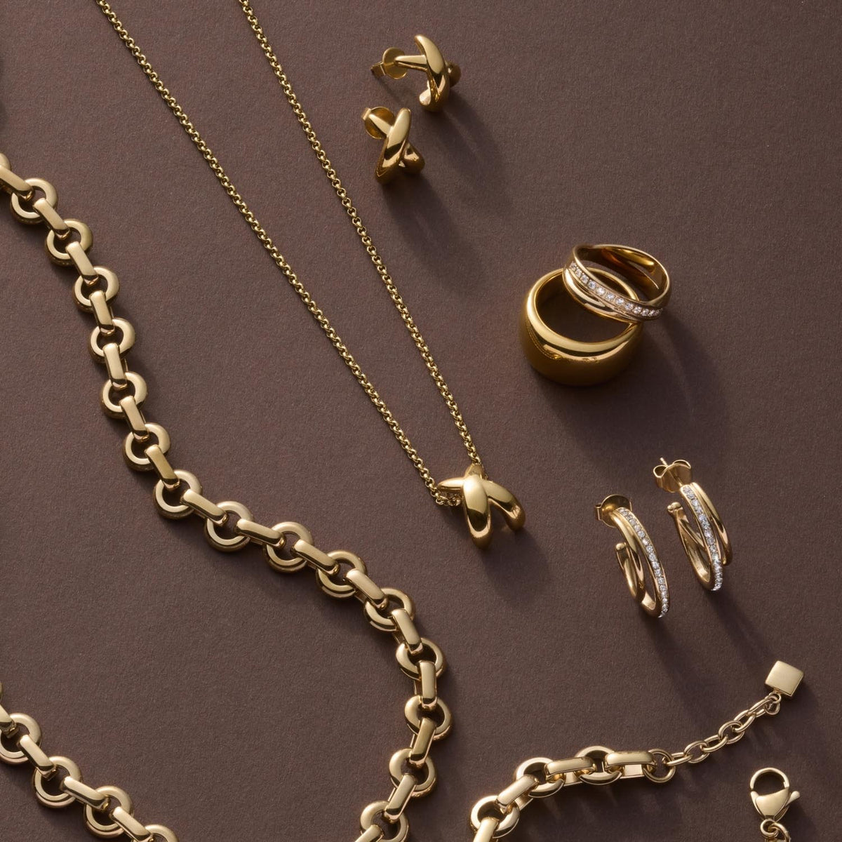 Goldene Schmuckkollektion mit Ringen, Ketten und Ohrringen auf braunem Hintergrund