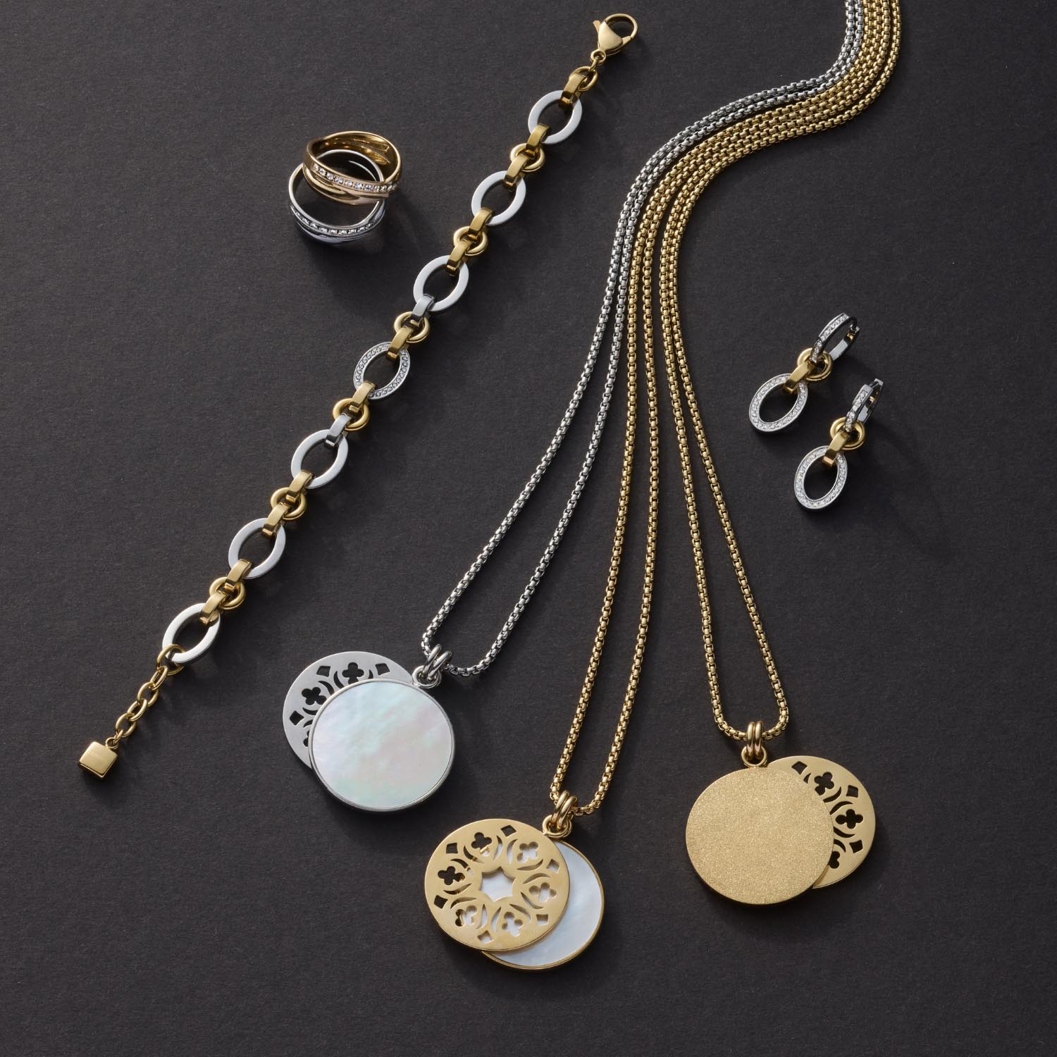 Schmuckkollektion mit Halsketten, Ring und Ohrringen in Gold und Silber auf grauem Hintergrund