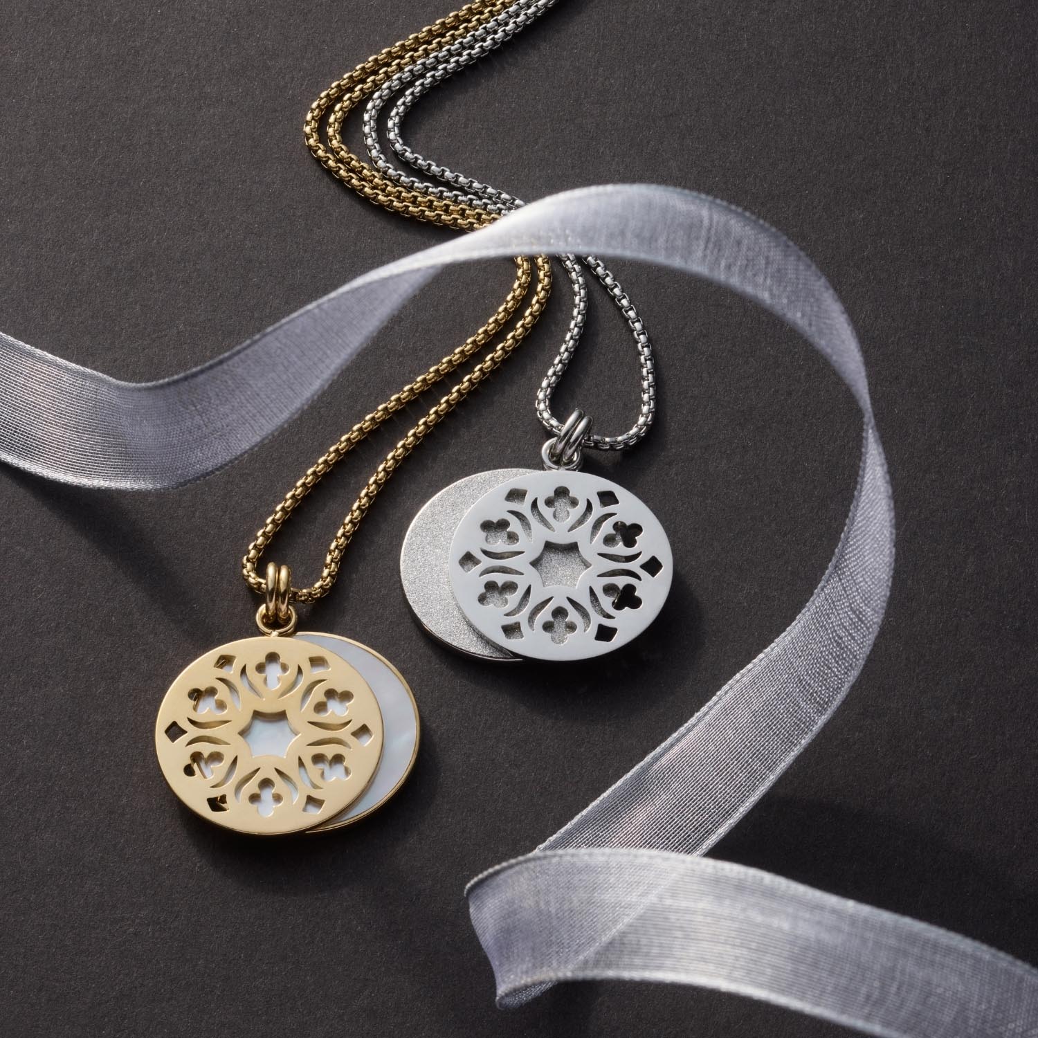 Zwei goldene und silberne Halsketten mit rundem Anhänger und ornamentalem Muster auf grauem Hintergrund